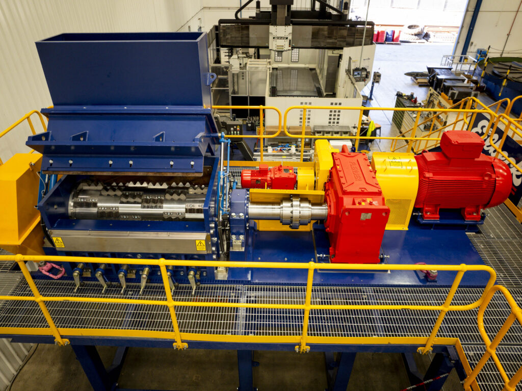 A blue shredder with a red drive and a yellow walkway on the workshop floor