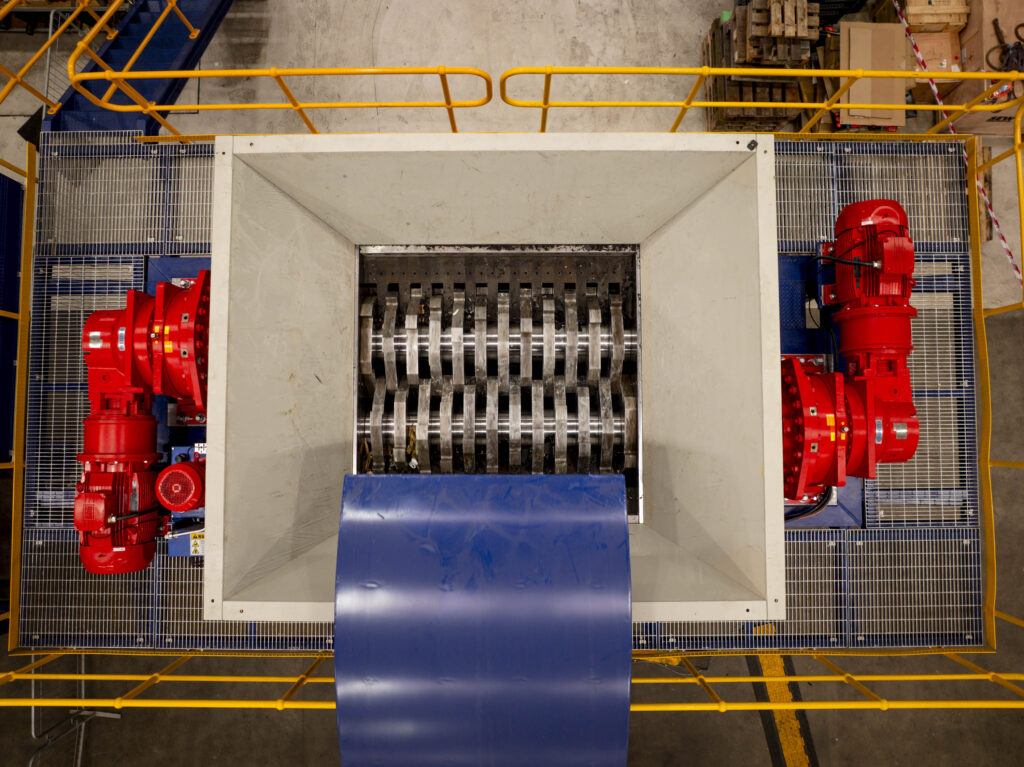 Looking down into the hopper of a dual-shaft shredder, with a red drive on each side