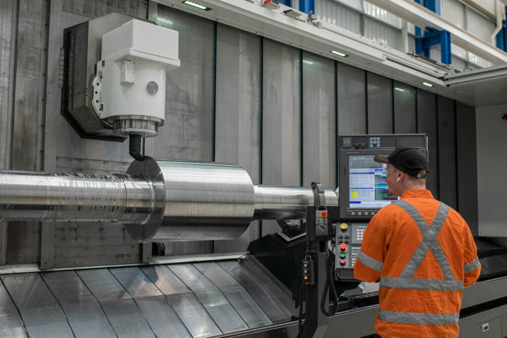 An operator machines a steel shaft on a horizontal boring machine