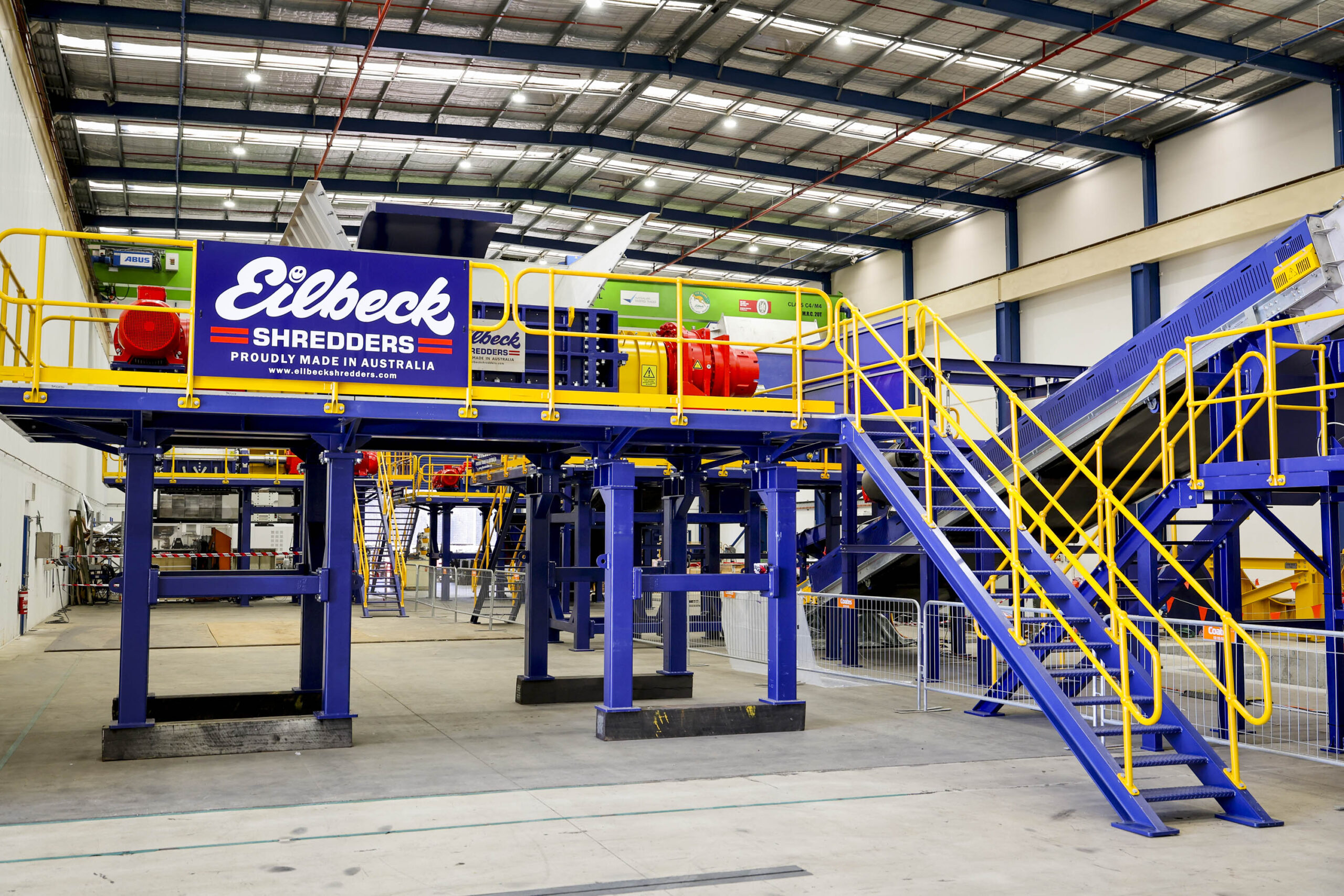 An Eilbeck Shredders line on its blue steel platform, with its yellow stairs and conveyor, in the Eilbeck workshop